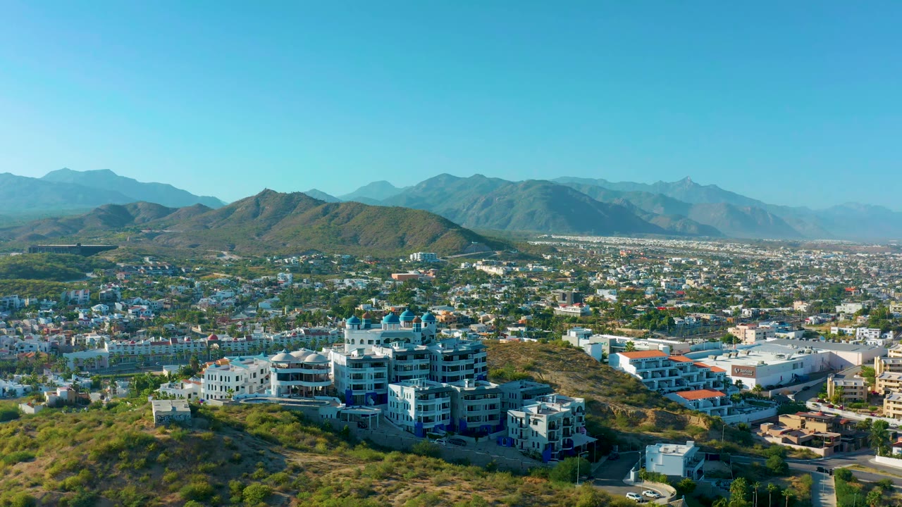 San Jose del Cabo hillside homes sit low in the frame while the city fills the middle distance, mountain ridges line the horizon, and no visible people appear.