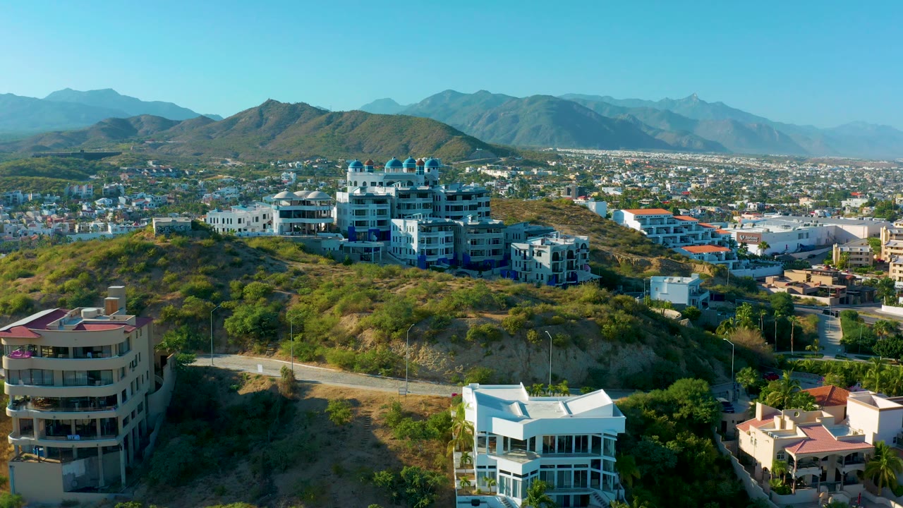 Hilltop residential buildings above a winding road with mountains behind the city.