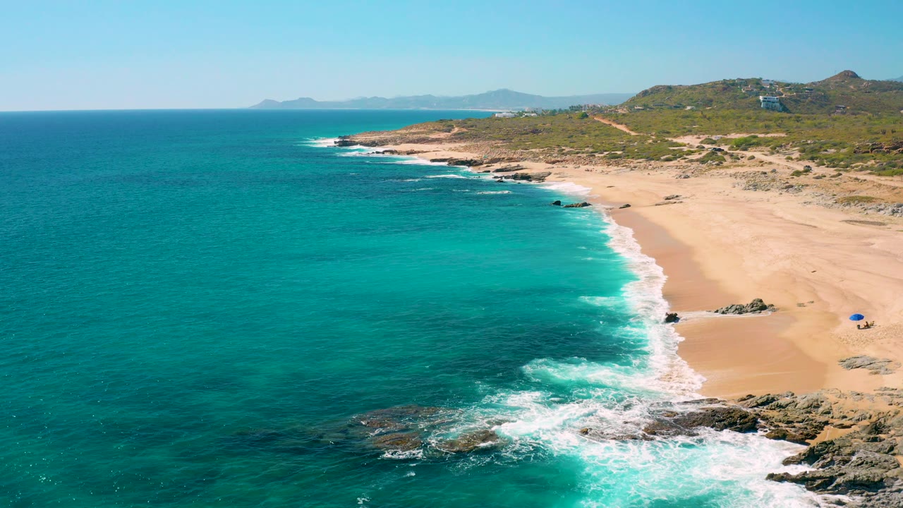 Aerial beach view with waves rolling onto sand and rocks.