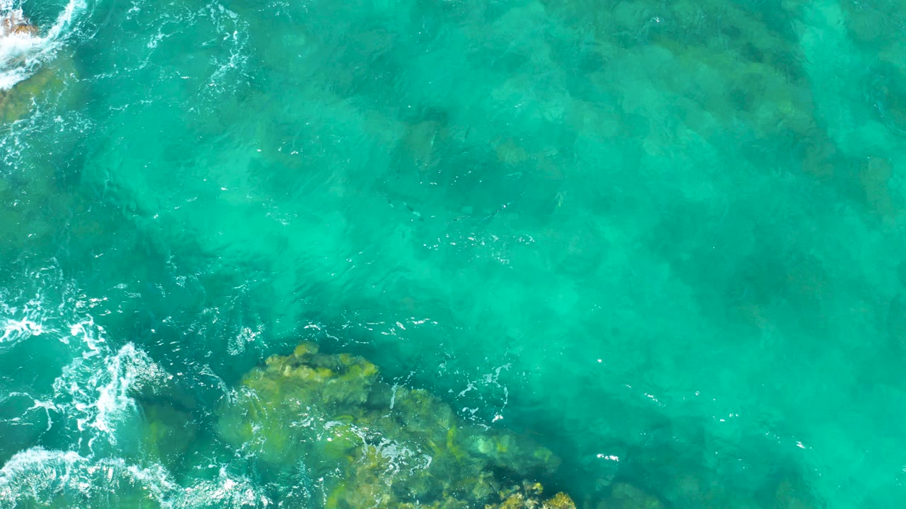 Turquoise ocean water over rocks with foam at the edge
