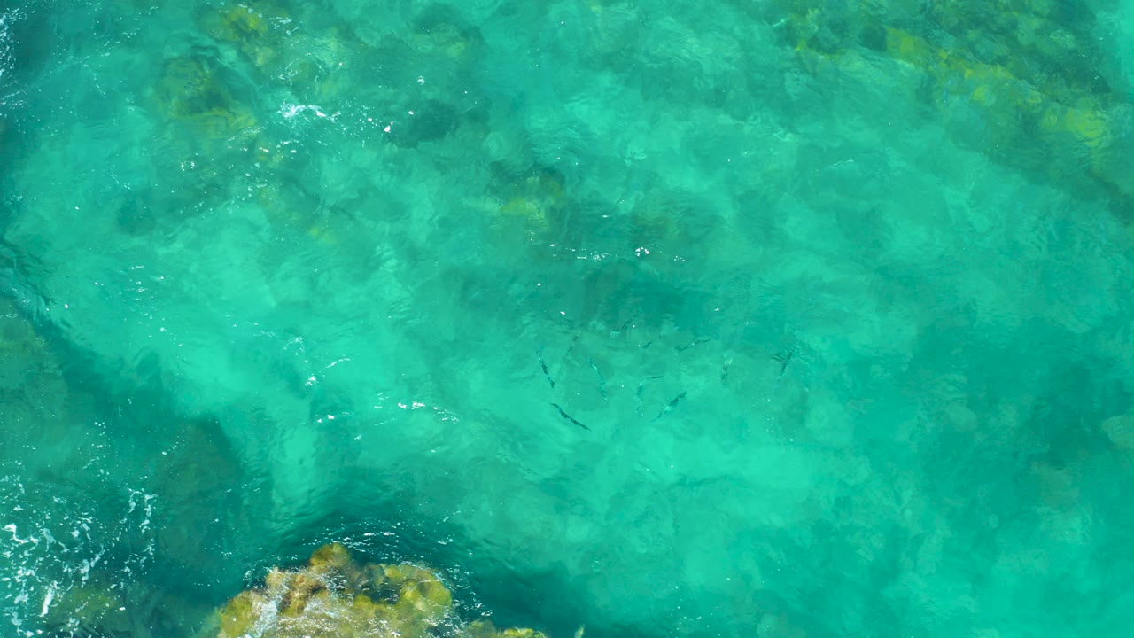 Turquoise water over a rocky seabed with foam near the edge.