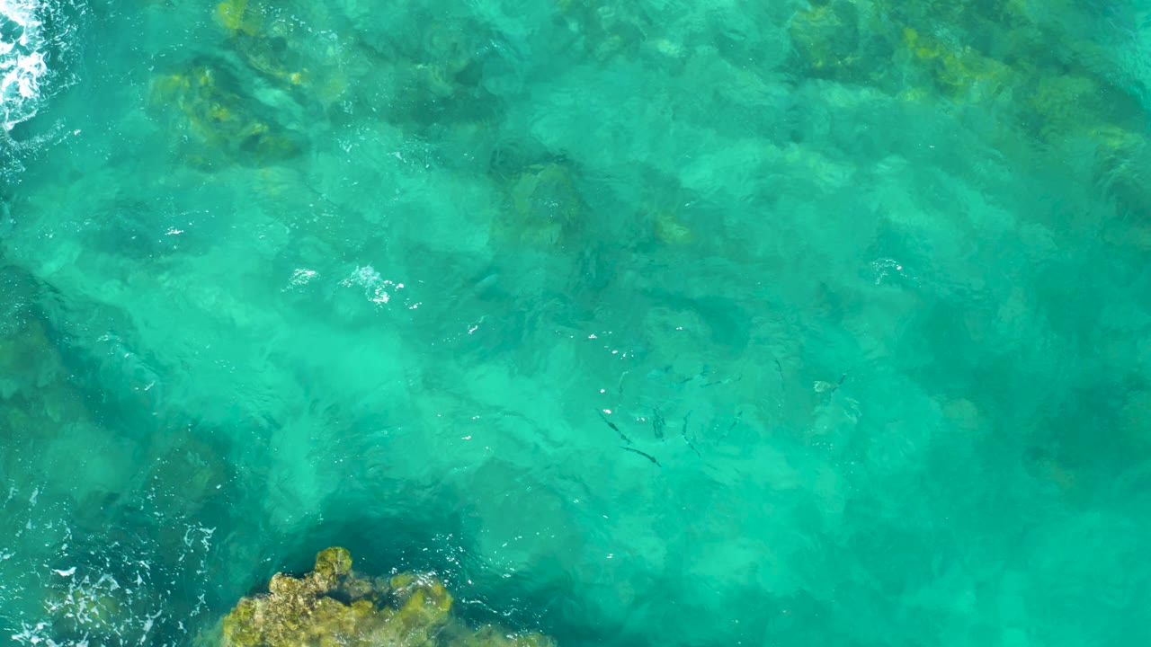 Top-down East Cape BCS Mexico water view with underwater rocks, a narrow white foam streak near the top edge, and no visible people.