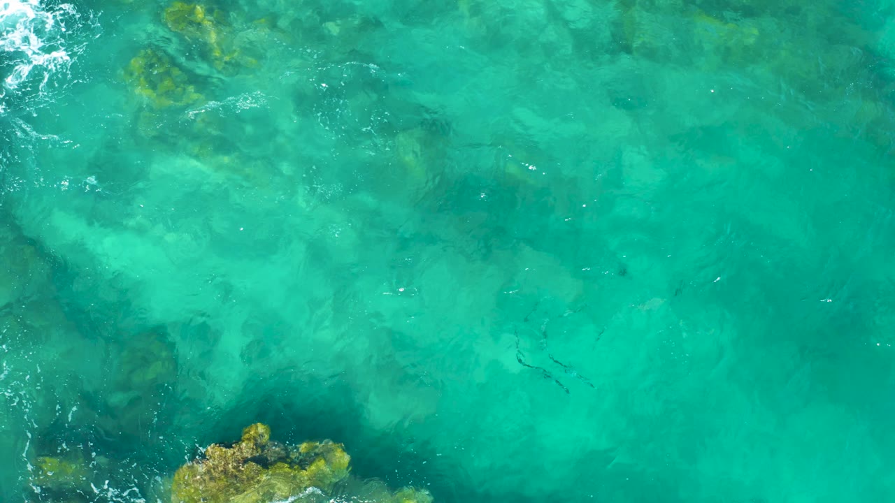 Overhead East Cape BCS Mexico frame with scattered rocks under clear water, white foam along the left edge, and no visible people.