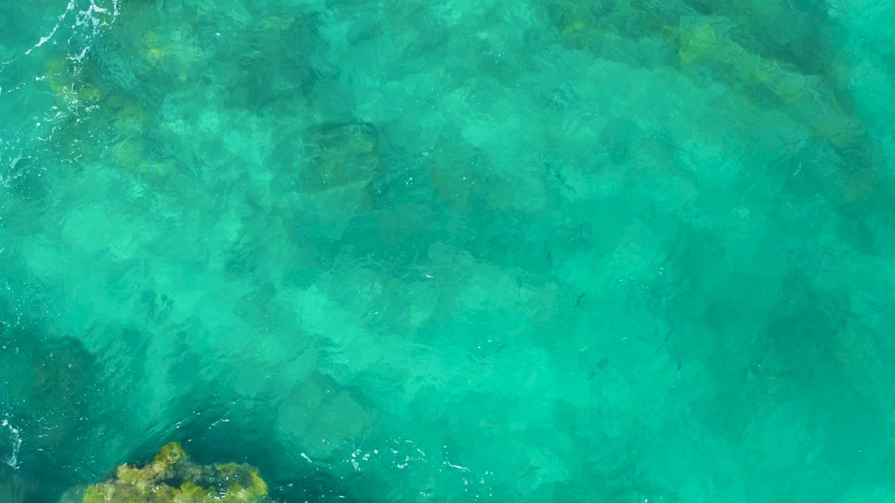 Top-down turquoise water with submerged rocks and small ripples.