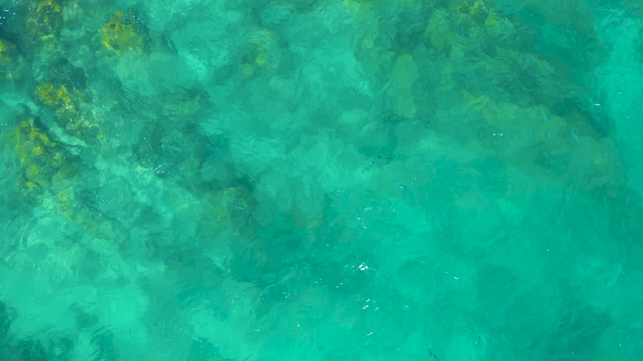 Turquoise East Cape BCS Mexico water fills the frame with darker underwater rock shapes and small bright ripple highlights, no visible people.