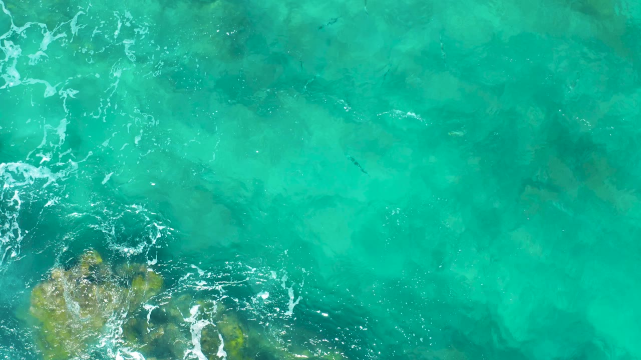 Shallow turquoise water with rock and coral texture entering from the lower left.
