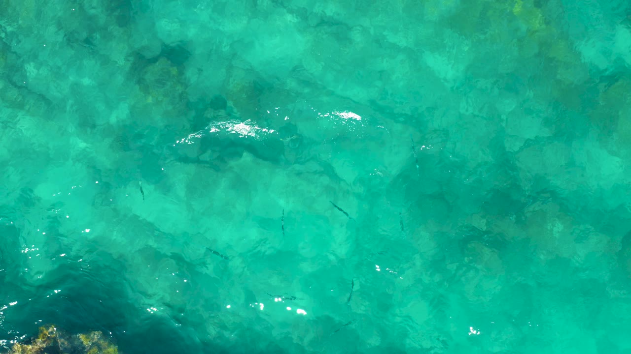 Shallow turquoise water in East Cape, Baja California Sur, with bright ripple highlights crossing darker seabed areas and no visible people.