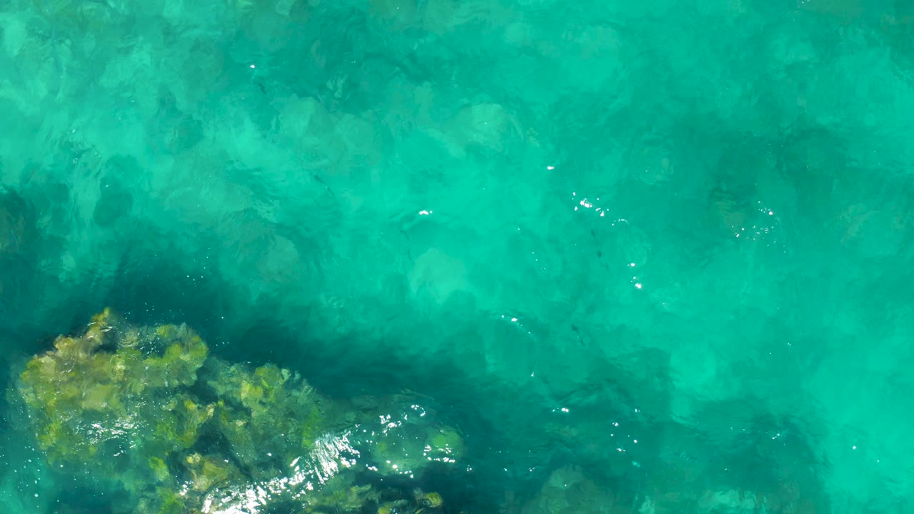 Clear turquoise water in Baja California Sur with a rocky seabed visible in the lower left and no visible people.