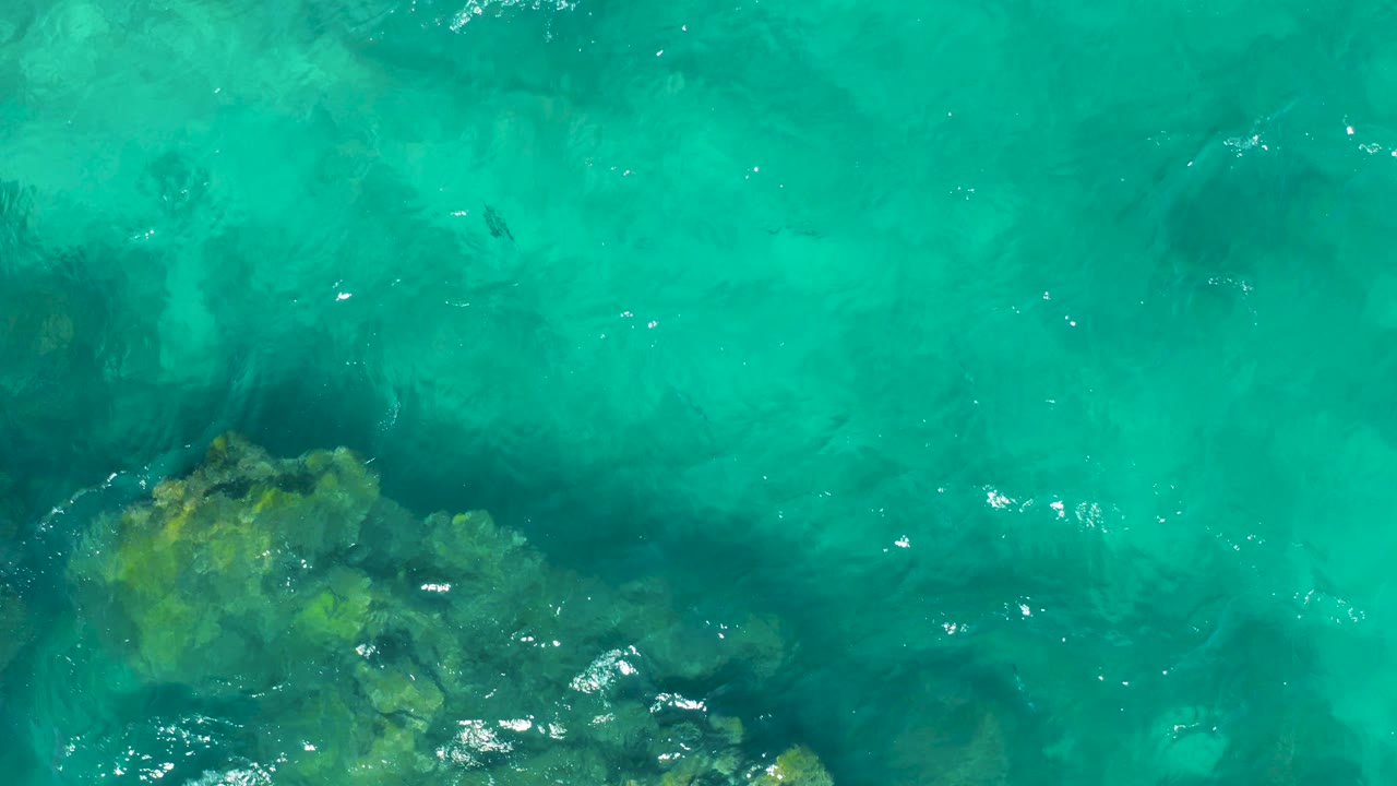 Clear turquoise water covers a rocky seabed that sits mainly in the lower left of the East Cape frame, with no visible people.