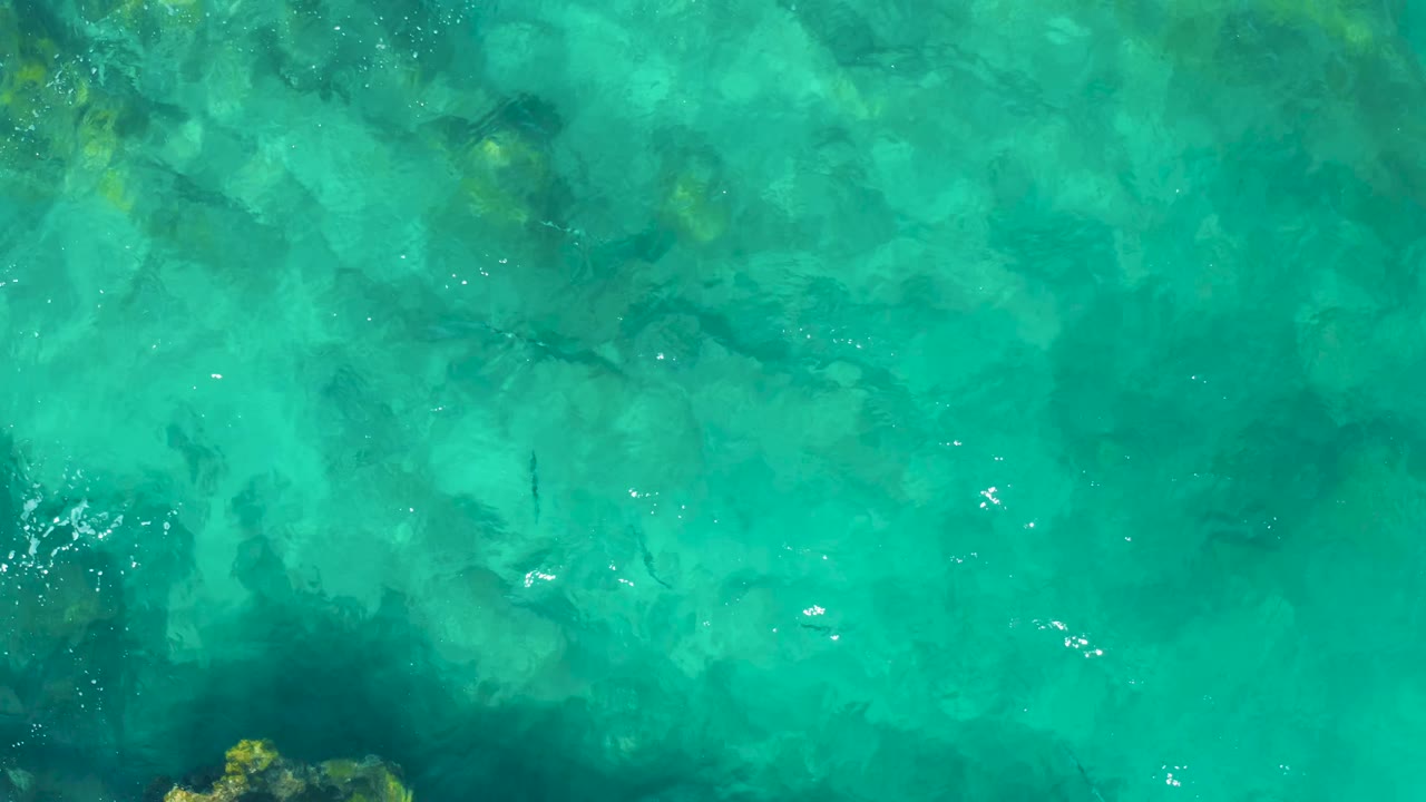 Clear green-blue water with darker submerged rocks