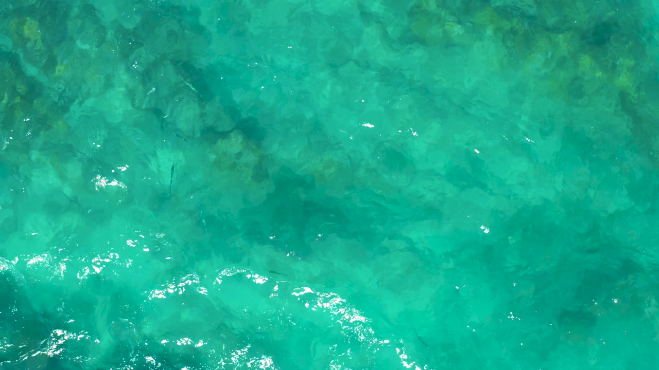 Clear green-blue ocean water fills the frame, with submerged rocks visible under soft ripples and no visible people.