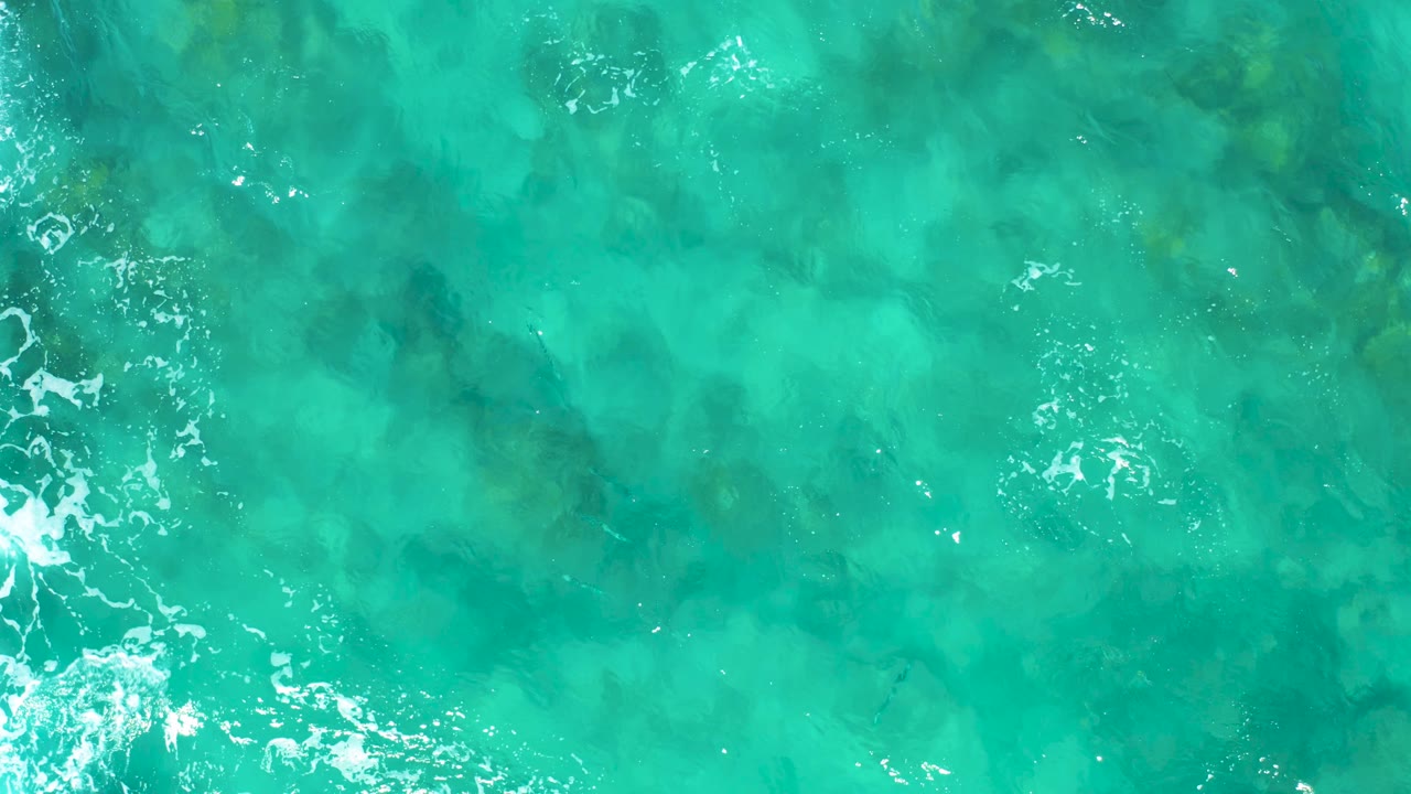 Overhead turquoise sea with a vertical band of white foam near center.