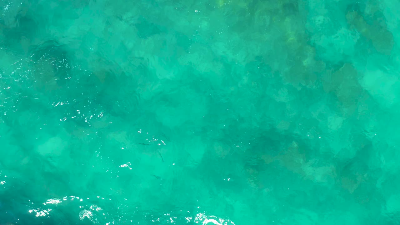 Clear green-blue shallow ocean water in East Cape, Baja California Sur, Mexico, with bright reflections scattered across the surface and no visible people.