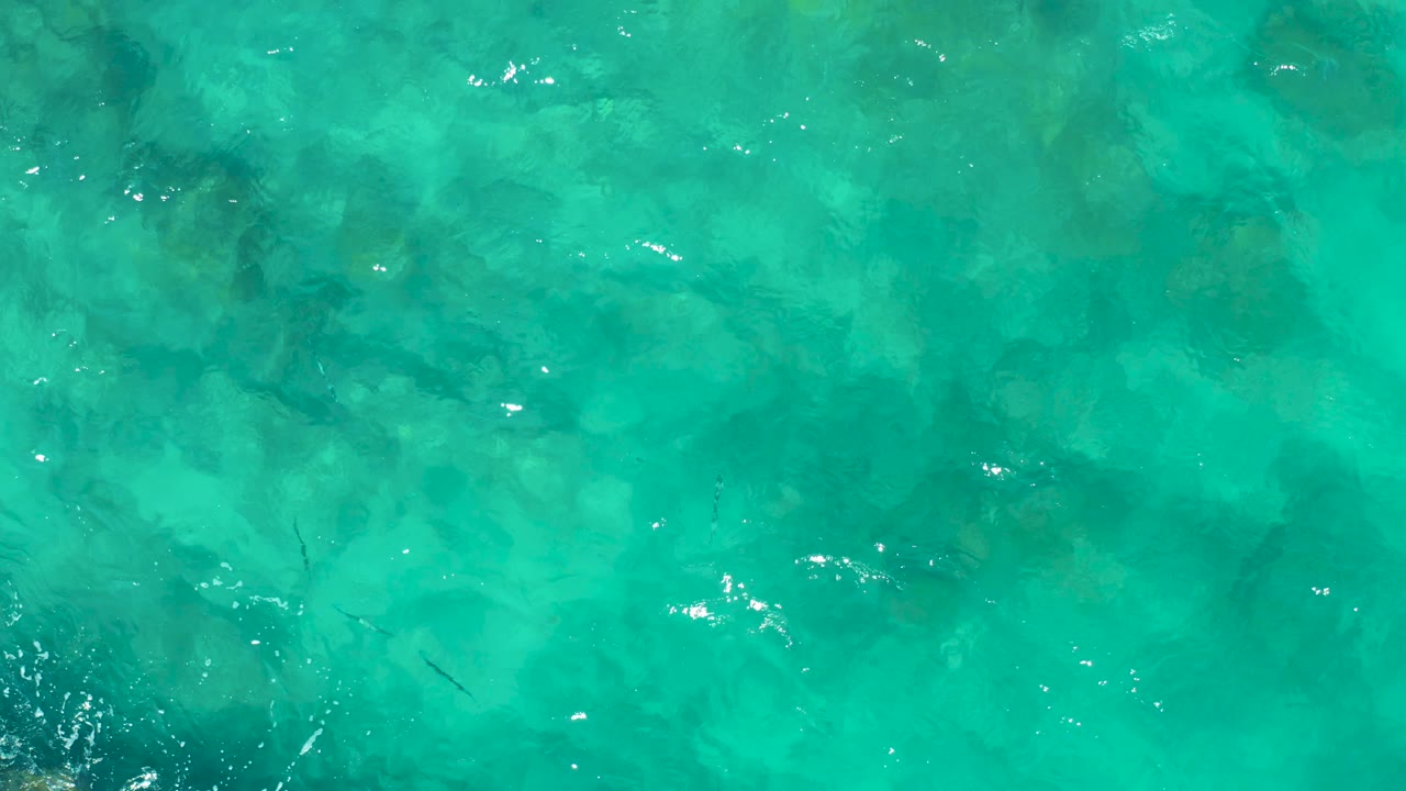 Shallow turquoise ocean water in East Cape, Baja California Sur, shows faint rock shapes under the surface, small fish marks, soft ripples, and no visible people.