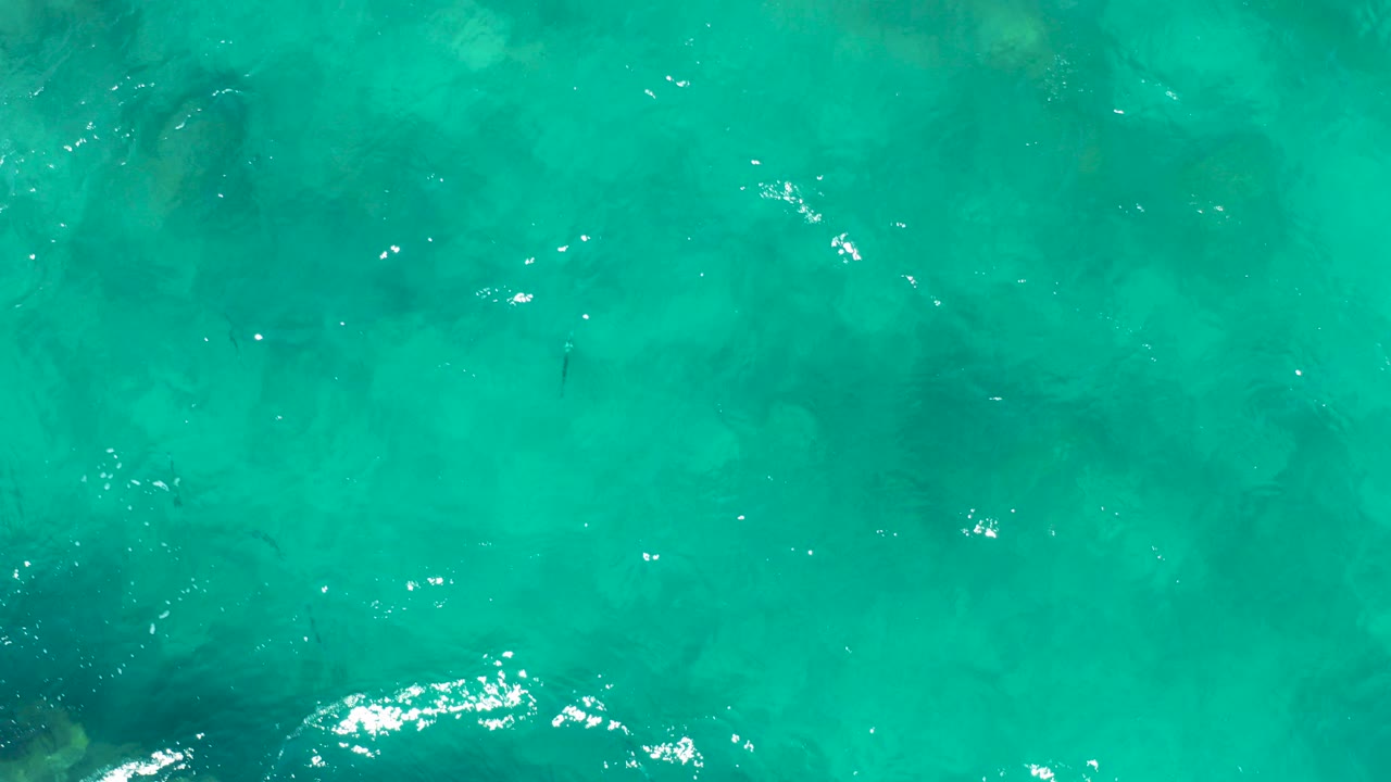 Turquoise ocean water with submerged rock shapes and small white wave highlights.