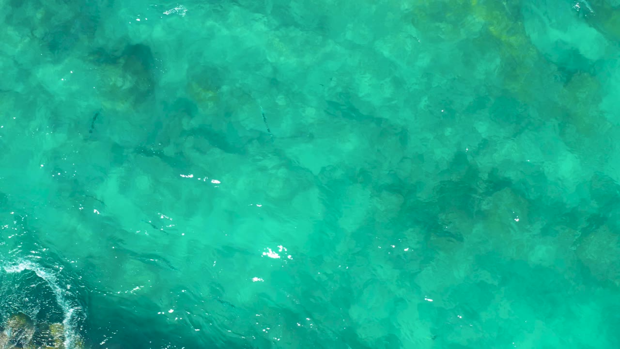 Aerial-looking view of shallow East Cape BCS Mexico water with visible rocky formations and small bright highlights on the rippled surface, no visible people.