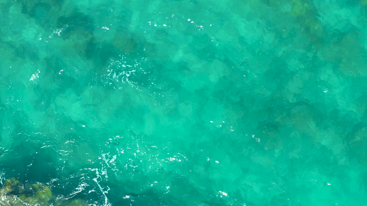 Overhead turquoise ocean water with dark underwater rocks near the lower left edge.