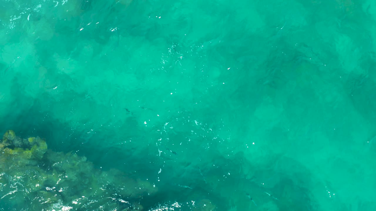 Clear shallow ocean water in East Cape, Baja California Sur, with faint rocky shapes below the turquoise surface and no visible people.