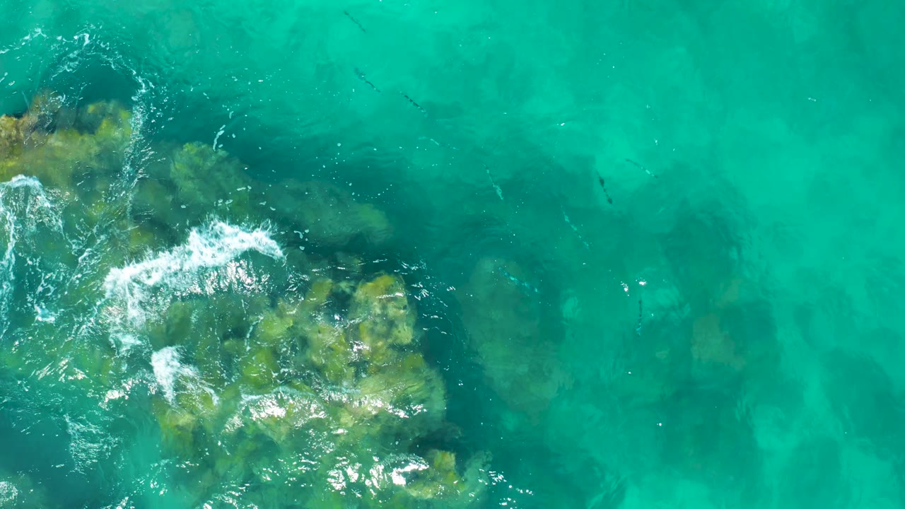 Overhead view of East Cape BCS Mexico water, with pale foam crossing the upper-left rock formation and open turquoise water to the right, no visible people.