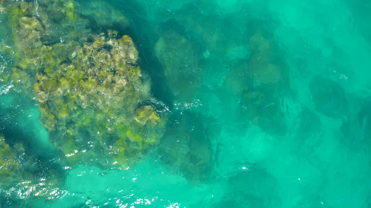 Top-down turquoise water over submerged rocky seabed.
