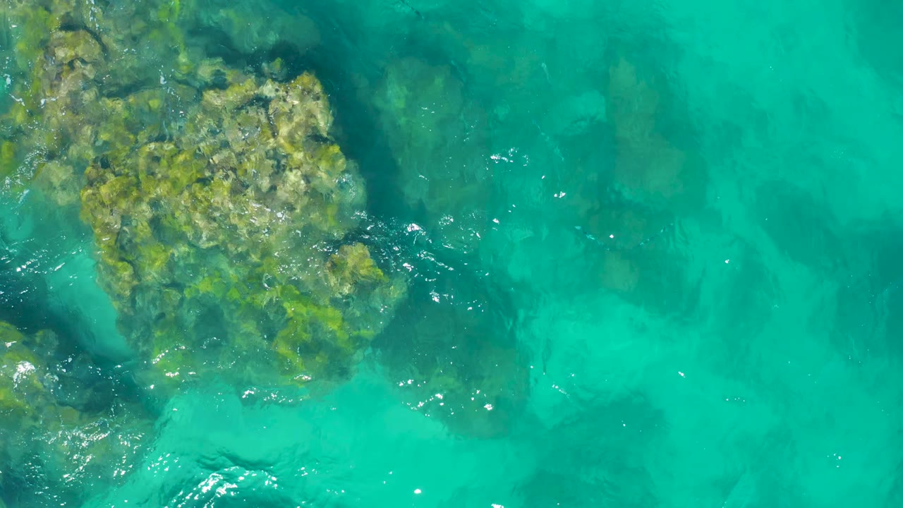 Top-down East Cape Baja California Sur water view with the rock cluster higher and more central, translucent turquoise water around it, and no visible people.