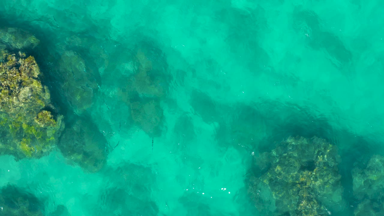 Overhead turquoise water with submerged rocks and coral patches.