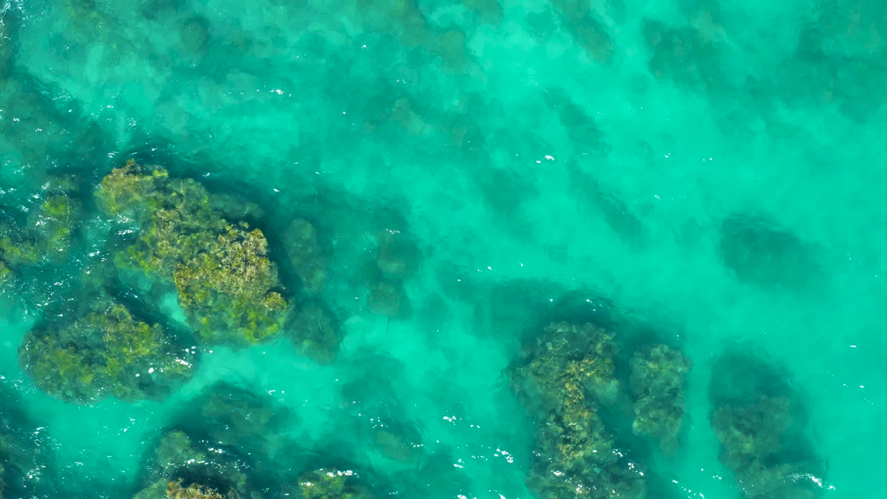 Aerial view of clear turquoise water around large submerged rock areas.