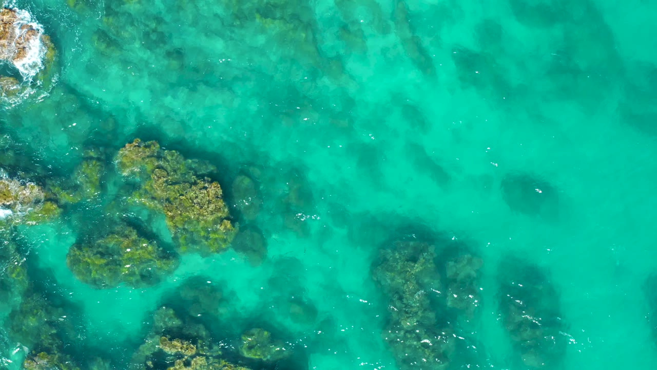 Turquoise ocean water over rocks with white foam near the edge.