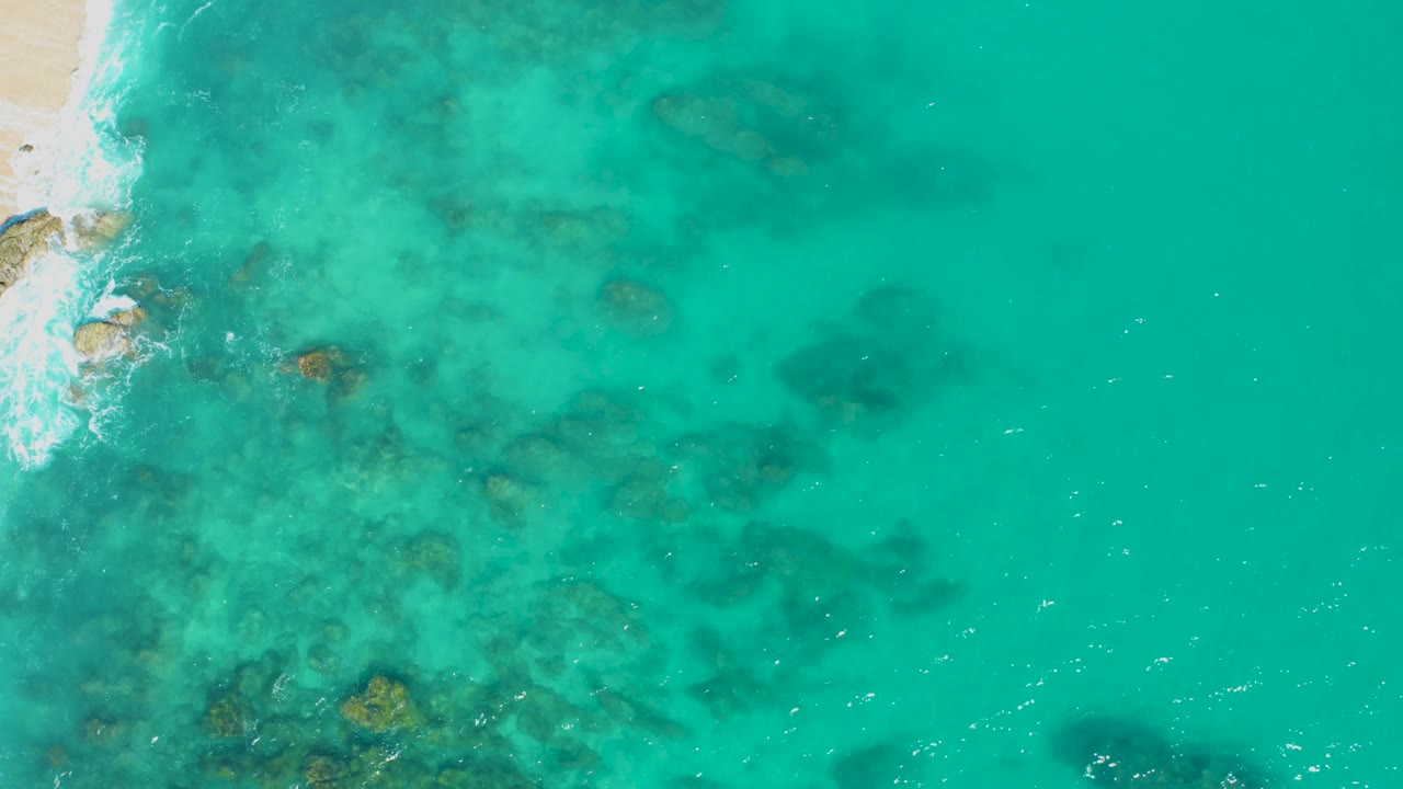 Shallow blue-green water with submerged rocks and sand at the left edge.