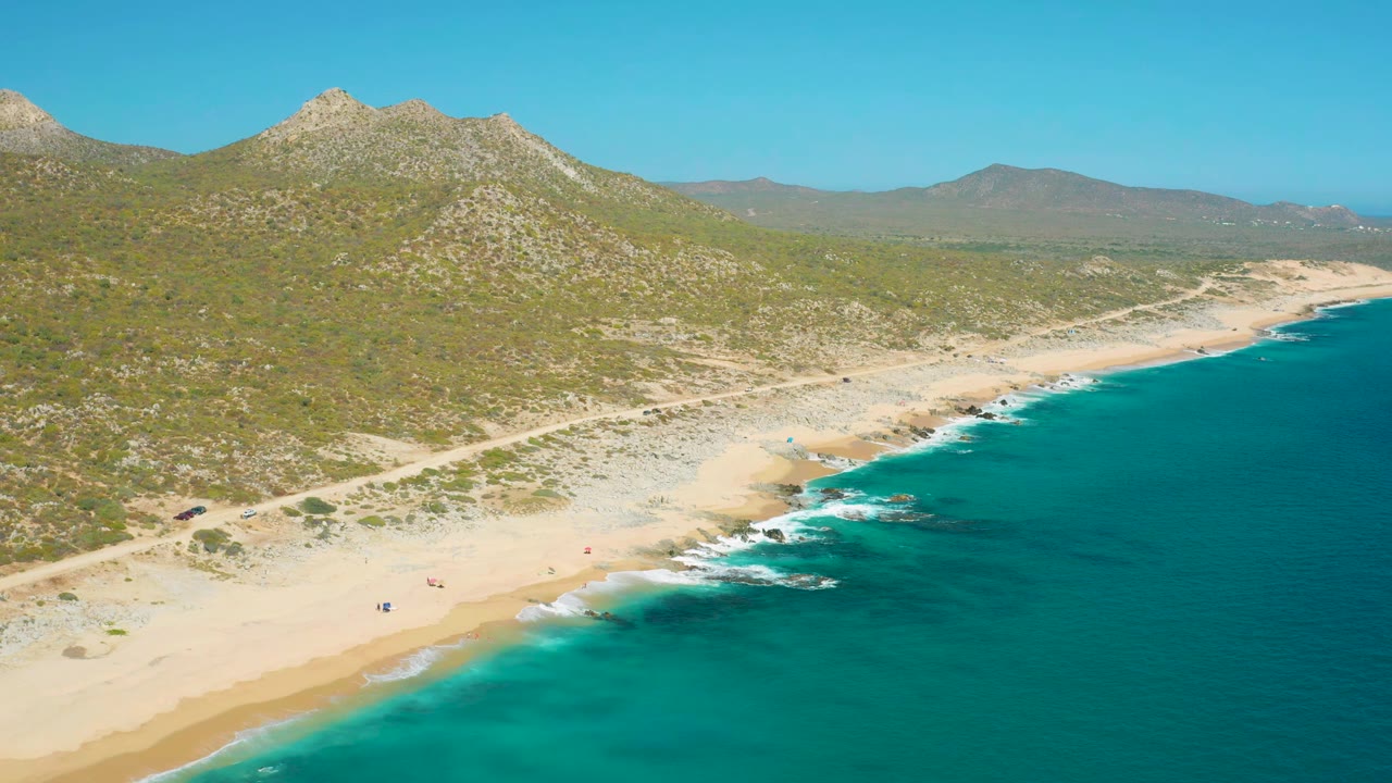 Wide drone view of turquoise surf beside a sandy shore.