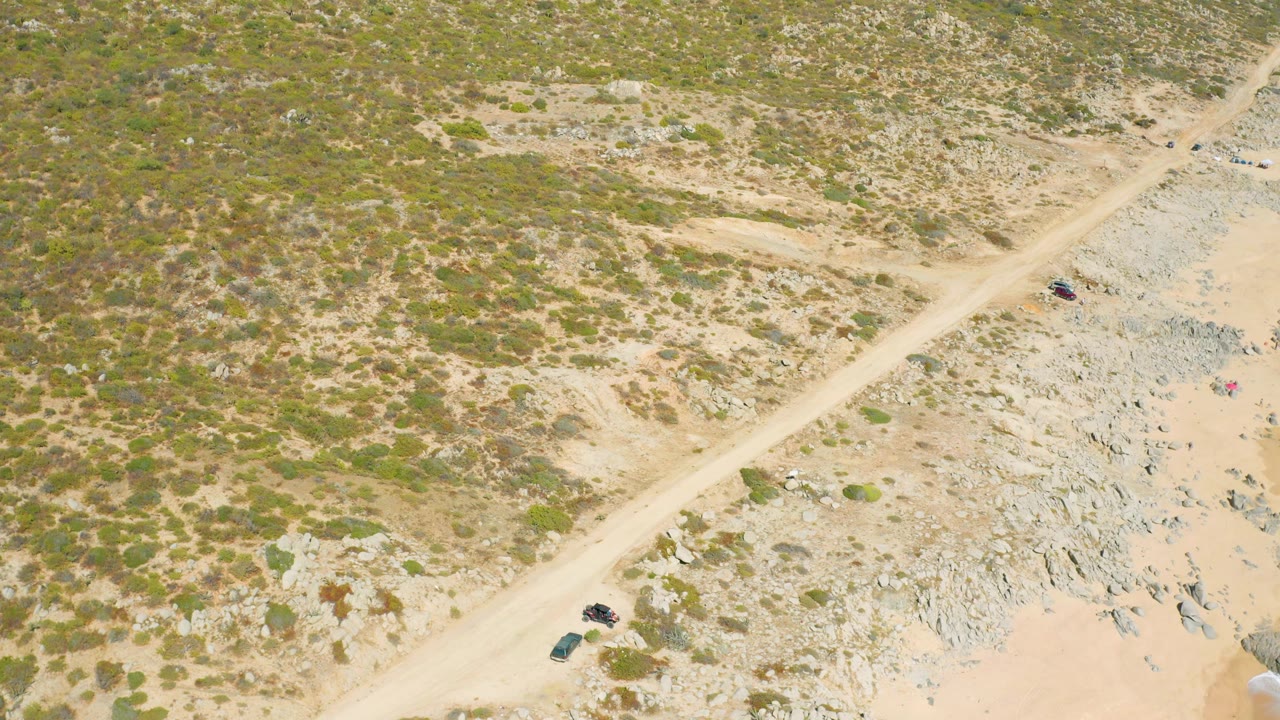 Aerial road scene with dry vegetation, rocks, and sandy ground.