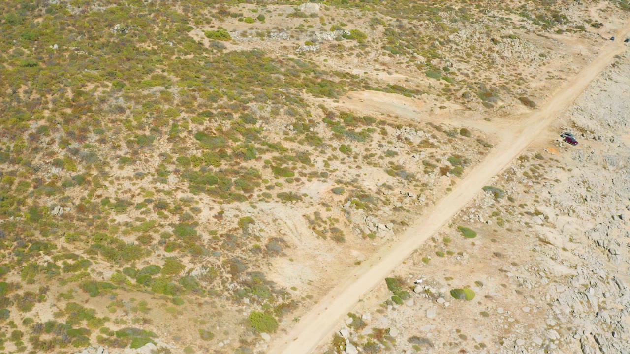 Aerial view of a dirt road crossing dry rocky scrubland with a small vehicle near the road edge.