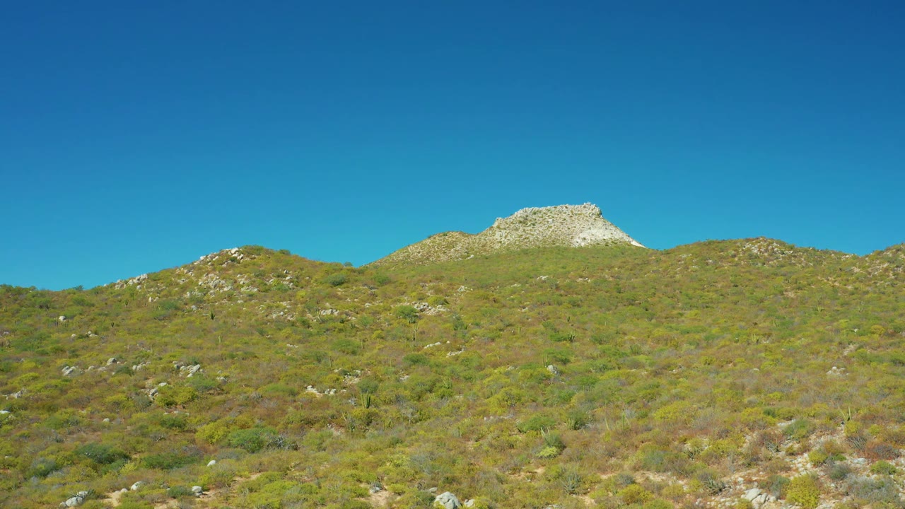 Third frame shows the same East Cape BCS Mexico slope with scattered rocks across the scrub, a pale ridge line near the top, clear sky, and no visible people.