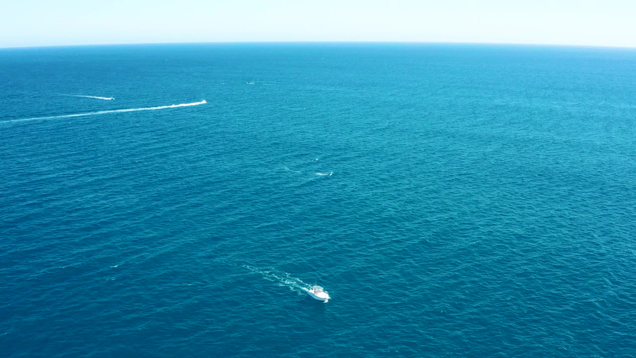 Aerial view over East Cape, Baja California Sur open ocean, with small boats leaving white wakes across blue water and no visible people.
