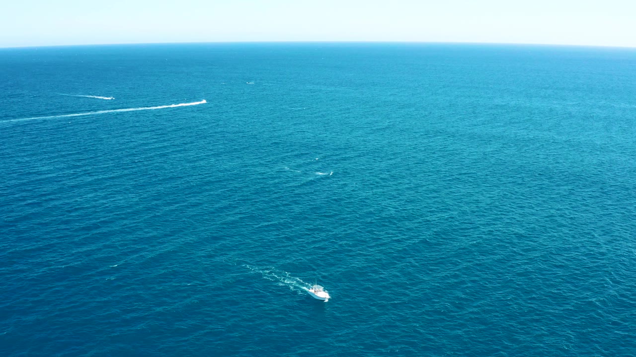 A small white boat moves across the lower part of the East Cape ocean view while longer wake trails sit near the horizon, with no visible people.