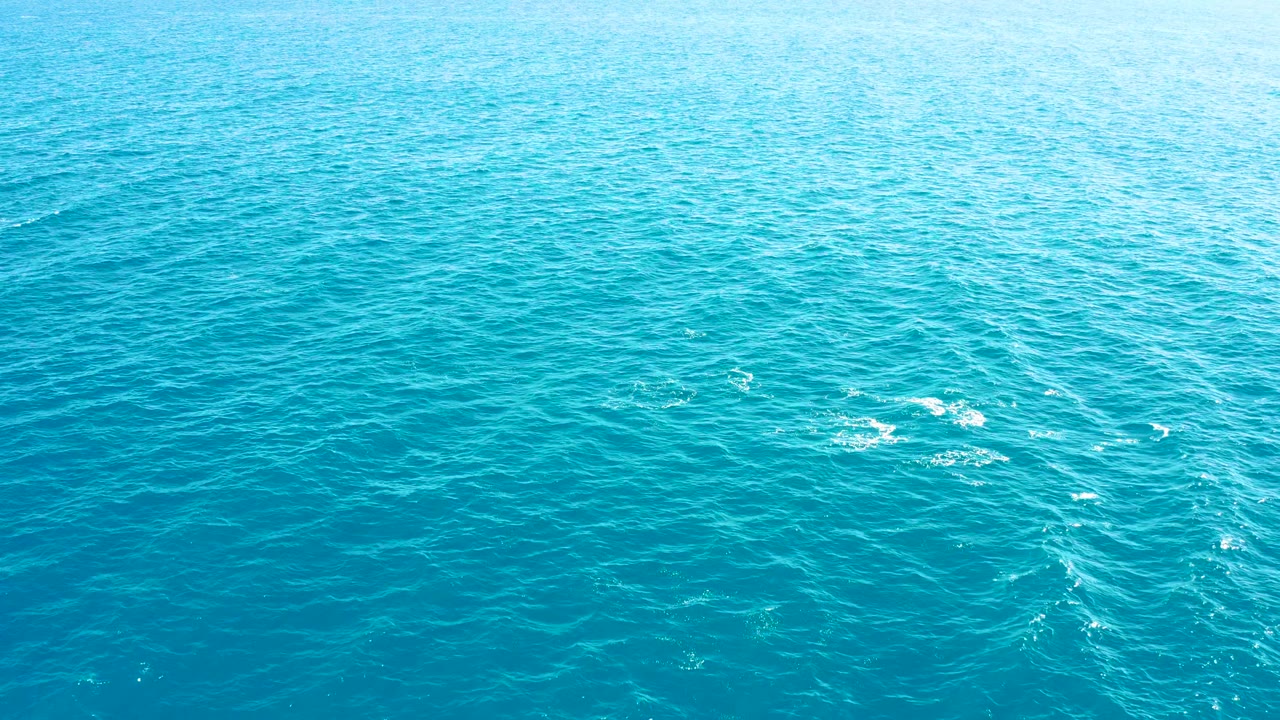 Overhead view of clear blue ocean in East Cape, Baja California Sur, with scattered white foam near the center-left and no visible people.