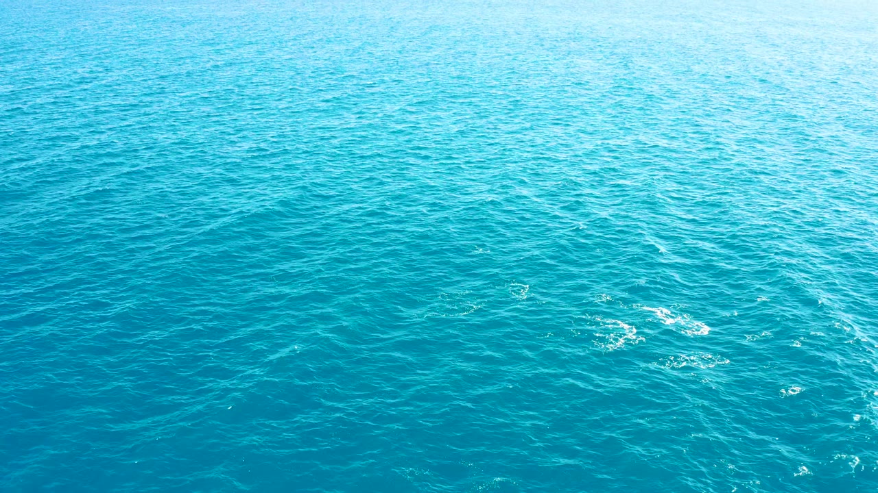 Turquoise ocean surface with foam near lower left