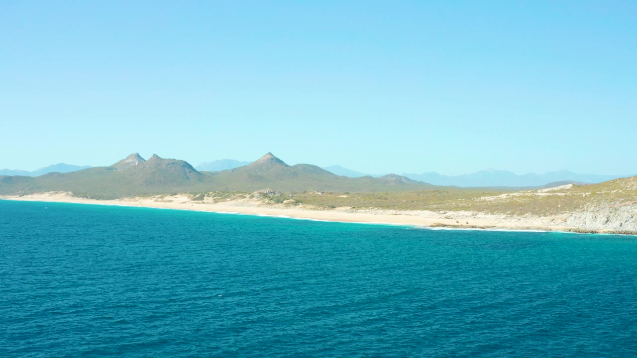 Turquoise ocean beside sandy beach and distant mountains