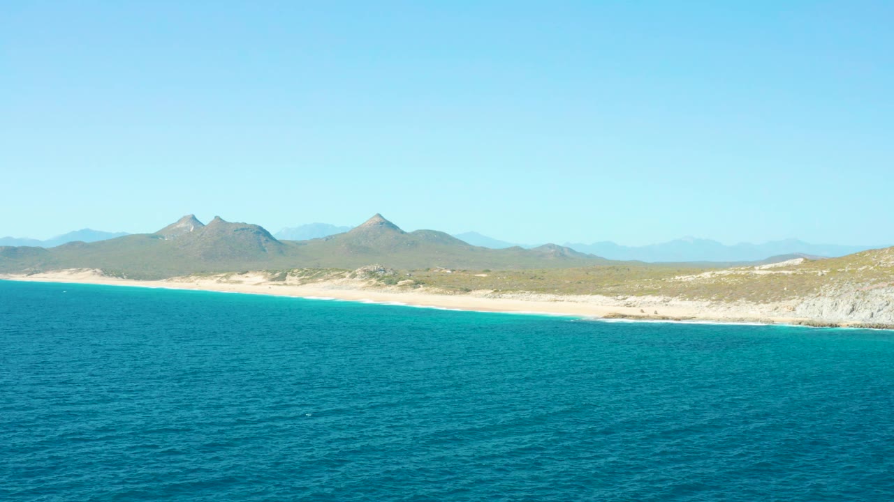 Second frame holds a similar East Cape coastal composition with blue water across the lower frame, beach and scrub in the middle, mountains behind, and no visible people.