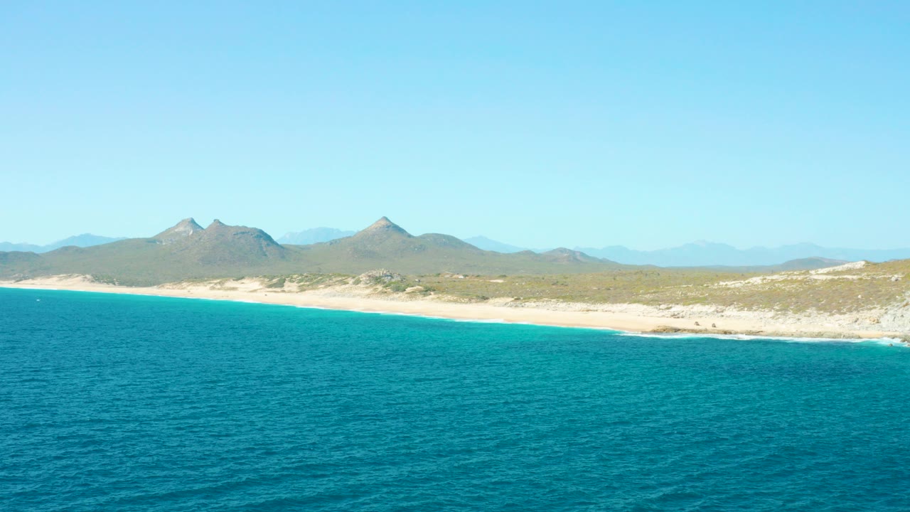 Turquoise ocean beside a sandy coast with distant mountains.