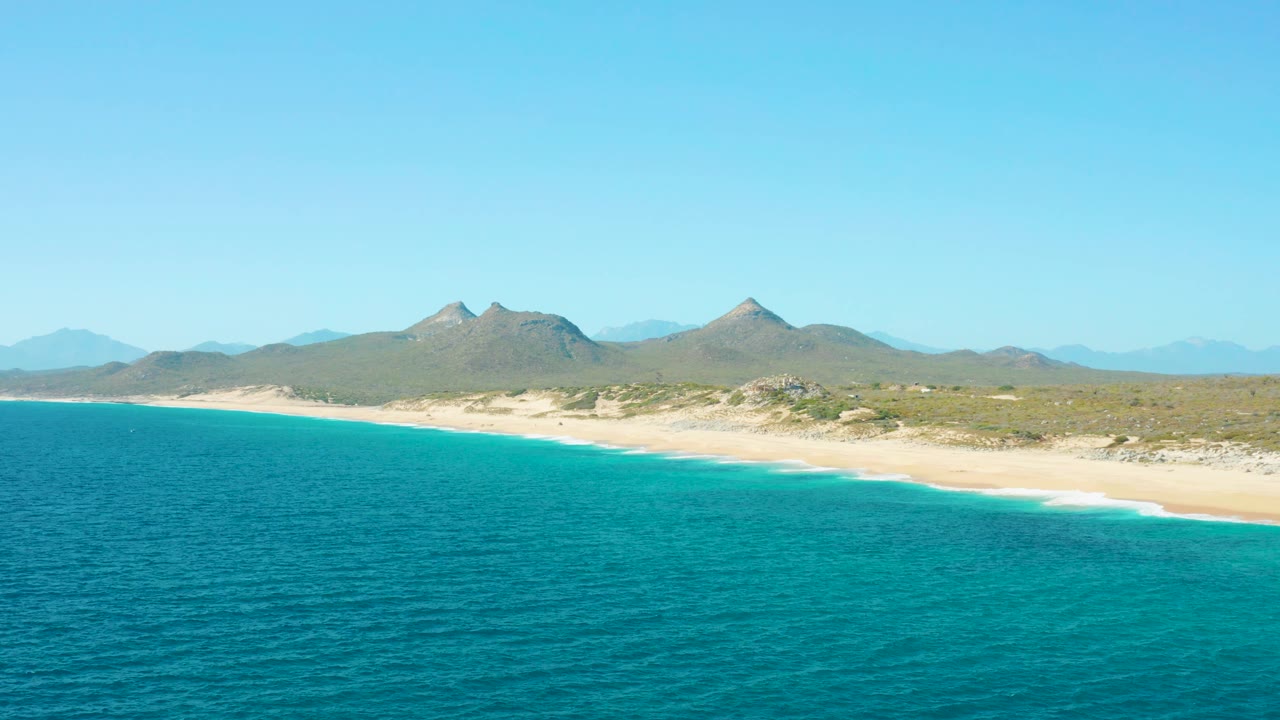 Beach coastline with gentle surf and clear mountain backdrop