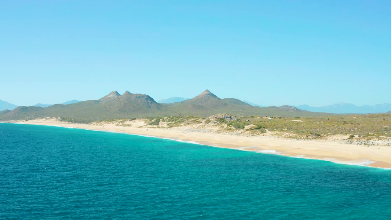Turquoise water and sandy beach below dry mountain ridges.