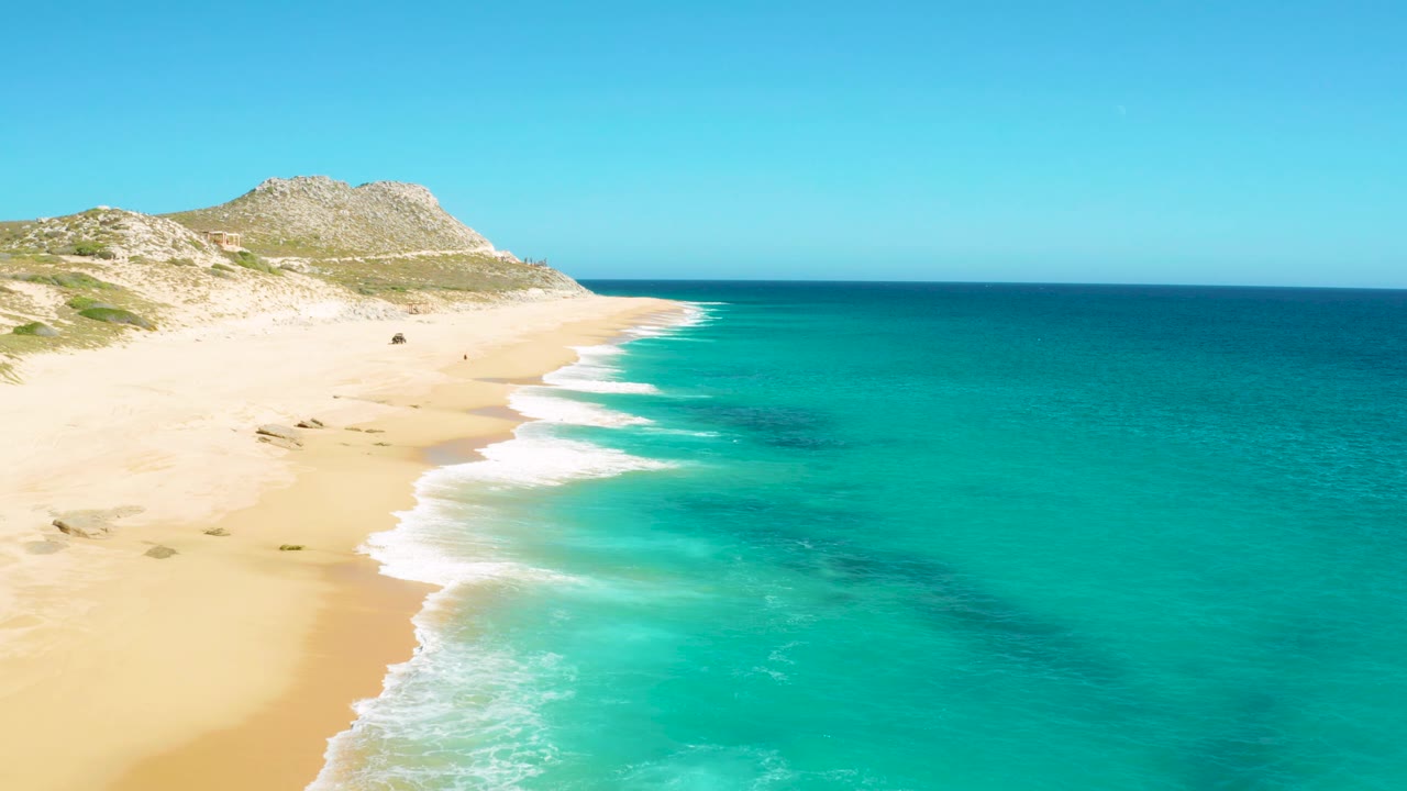 East Cape BCS Mexico coast with more shoreline visible down the left side, repeated white surf bands along the sand, turquoise water filling the right side, and no visible people.