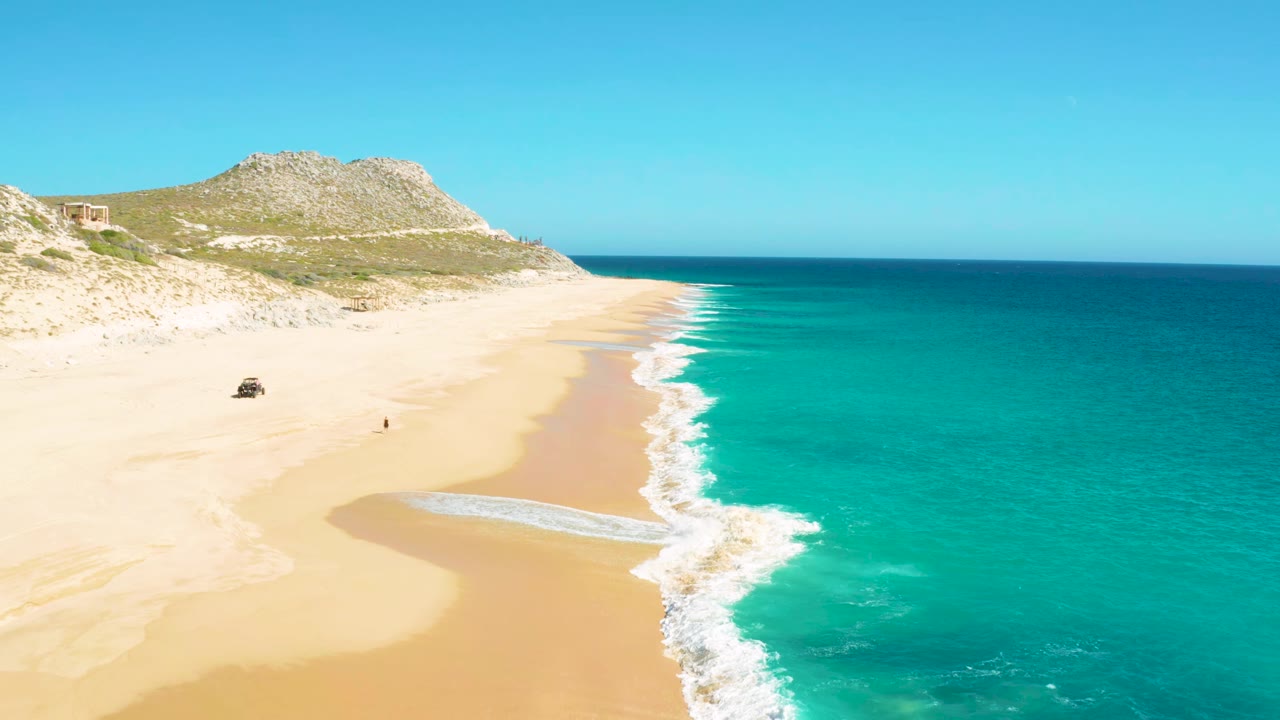 High aerial view of beach surf with a 4x4 and lone person on sand.