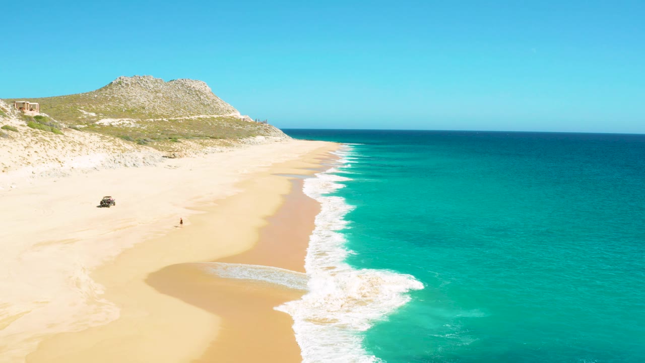Aerial view in East Cape BCS Mexico where a white wave pushes farther up the sand, with the 4x4 and lone walker remaining small against the open beach.