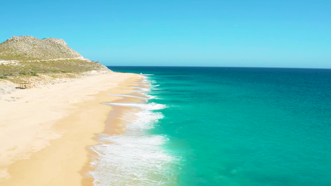 Aerial coastline view with sandy beach at left and turquoise sea at right.