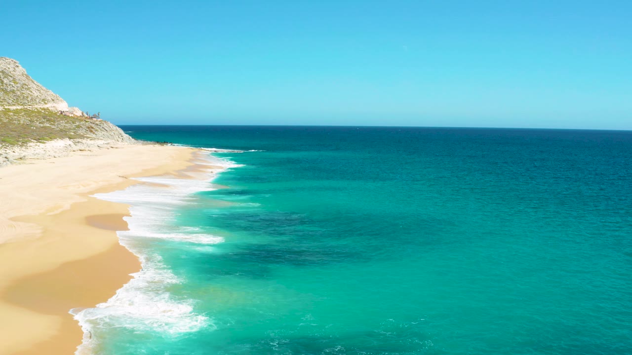 Drone view of beach surf curling beside clear turquoise and blue ocean water.