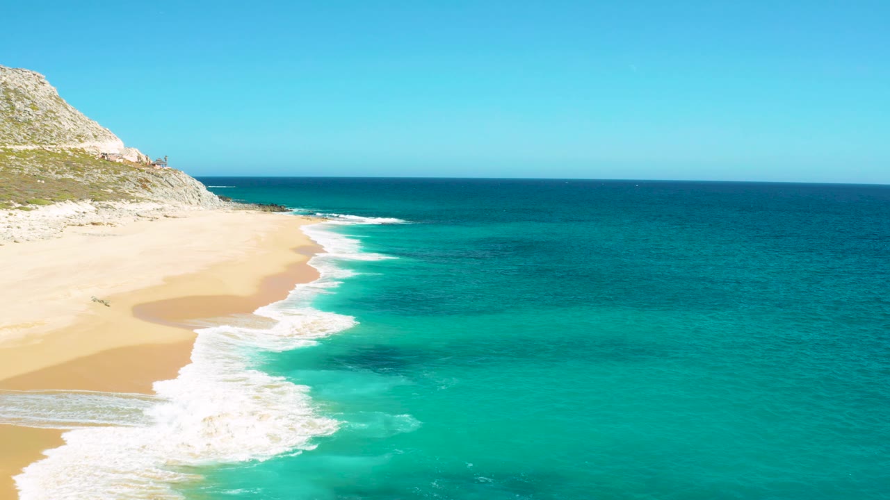Oblique aerial view of a sandy beach with waves sliding along the shore.