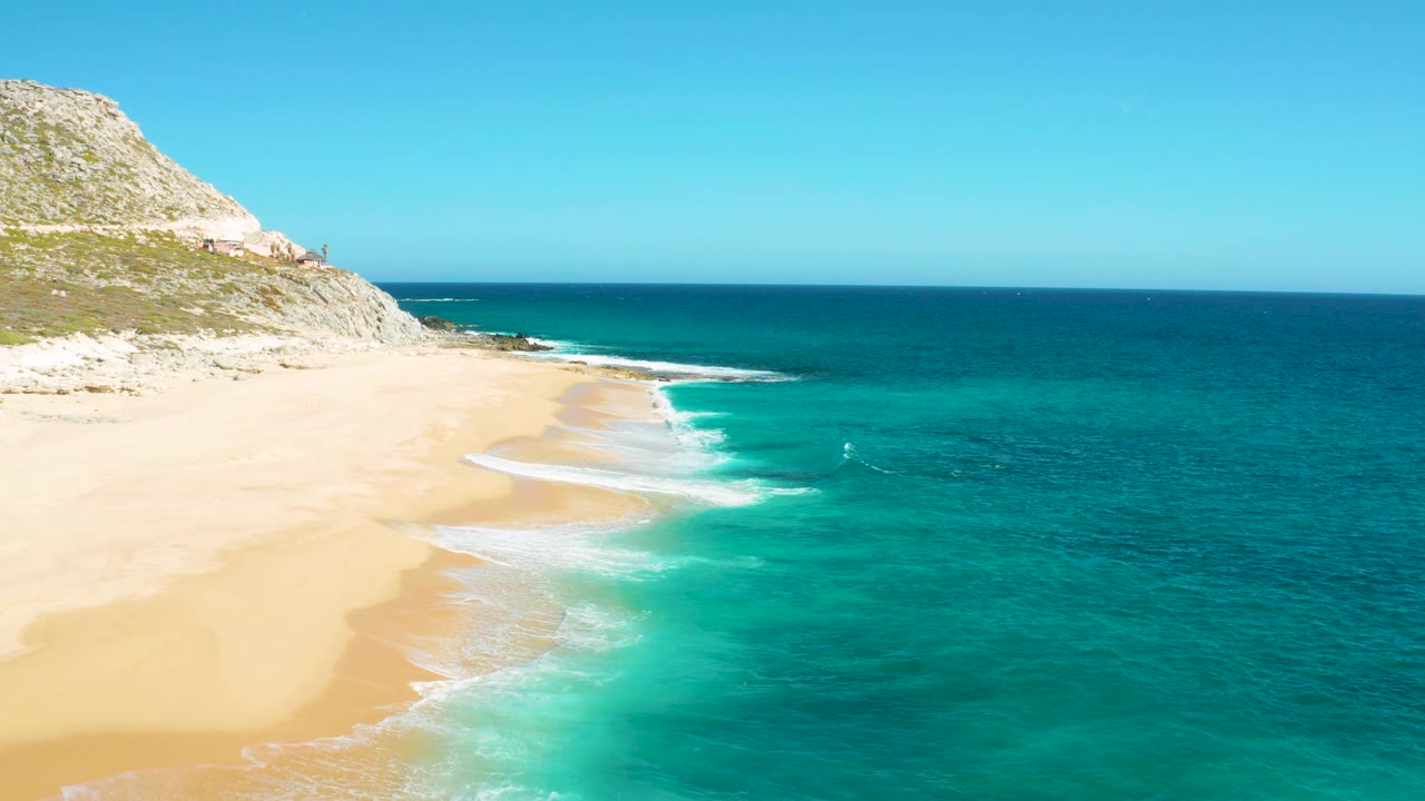 East Cape, Baja California Sur appears from above with pale sand dominating the left side, layered white surf lines crossing the middle, turquoise sea at right, and no visible people.