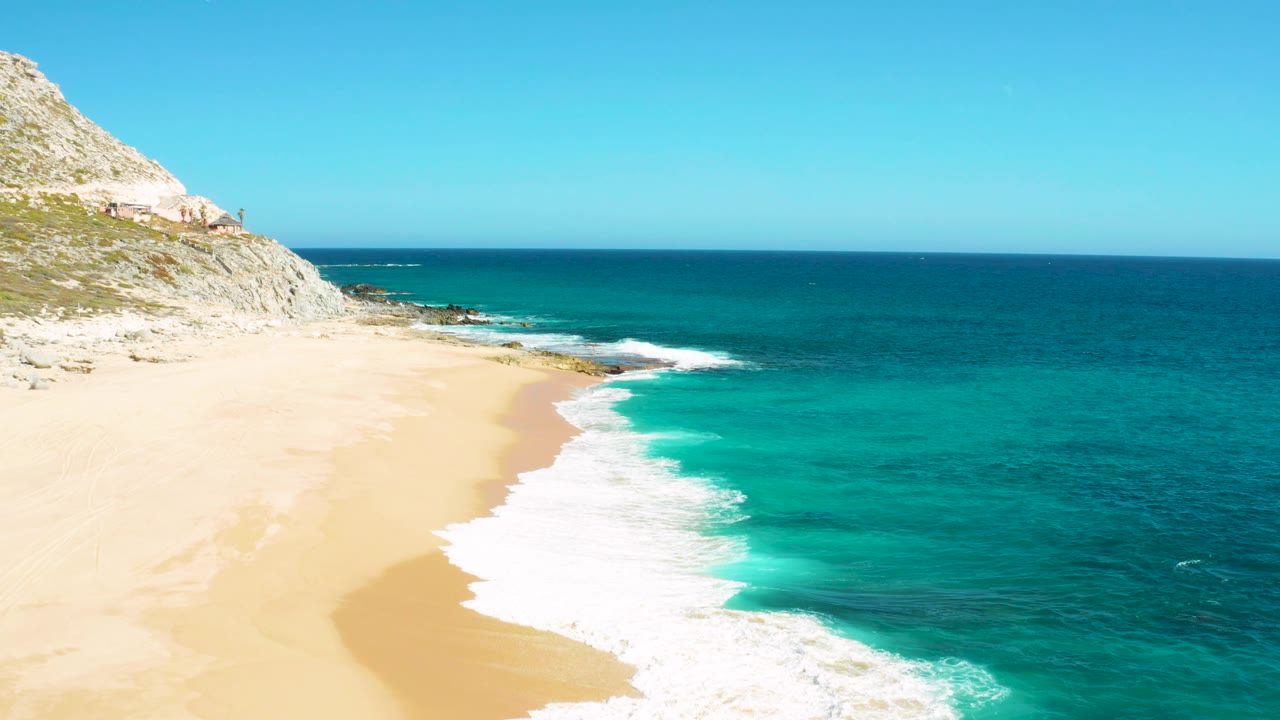 A larger sheet of white foam pushes onto the sand beside clear turquoise water.